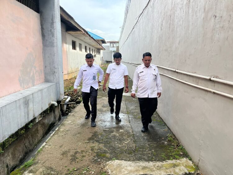 Kepala Urusan Umum (Kaur Umum) Lapas Kelas IIB Padangsidimpuan, Baginda Nauli Ritonga (paling kanan), bersama stafnya, melaksanakan pengecekan rutin kondisi fisik bangunan dan area drainase di jalur branggang Lapas.(Doc/Foto : Humas Lapassid)